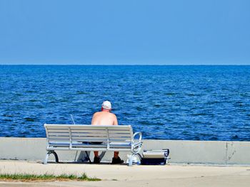Rear view of man sitting on bench against sea