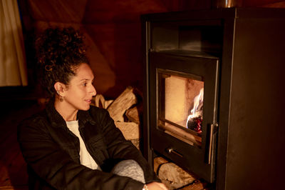 Relaxed woman sitting next to fireplace.