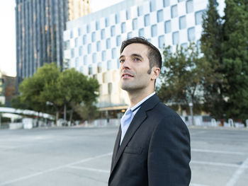 Side view of confident elegant adult male manager in formal suit standing near modern building on city street and looking away thoughtfully