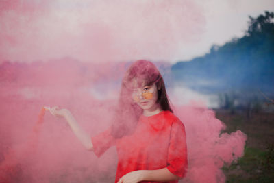 Portrait of young woman holding flaming torch emitting pink smoke