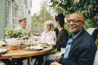 Portrait of smiling bald senior man sitting with friends at dining table during dinner party