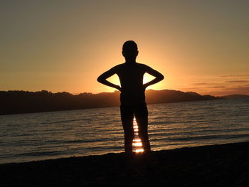 Silhouette man standing on beach against sky during sunset