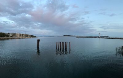 Wooden posts in sea against sky