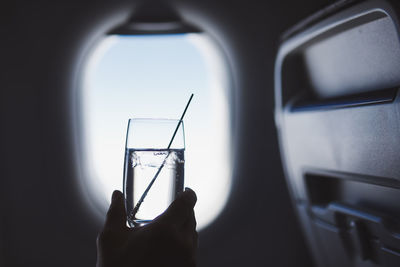 Passenger enjoy drink during flight. man holding glass of gin and tonic against airplane window.