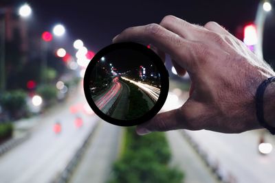 Close-up of hand holding lens against city at night