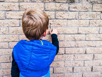 Rear view of boy in blue hooded shirt drawing on wall