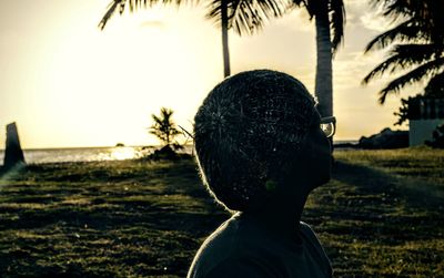 Palm trees on grassy field against sky at sunset