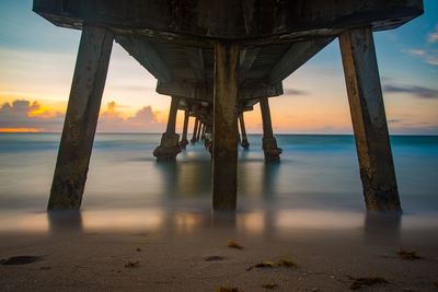 Underneath view of pier over sea during sunset