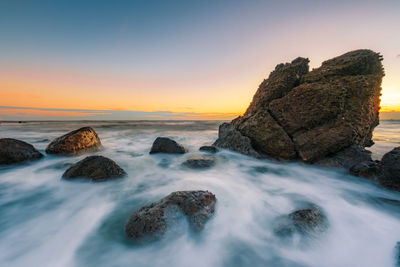Rocks in sea against sky during sunset