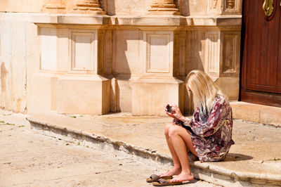 Full length of woman sitting outside historic building