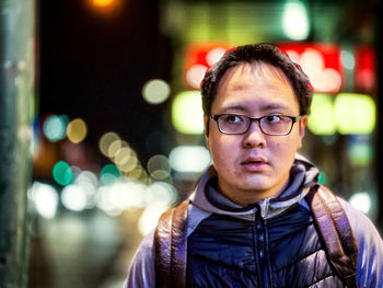 Portrait of young man wearing eyeglasses against neon lights at night.