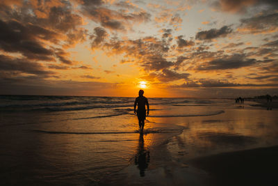 Silhouette woman walking at beach against sky during sunset