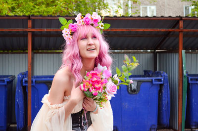 Portrait of smiling young woman holding bouquet against the backdrop of trash