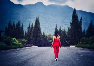 Rear view of woman walking on road leading towards mountains