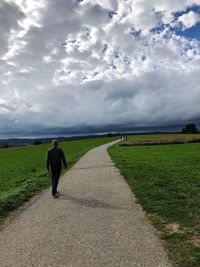 Rear view of man walking on road amidst field against sky