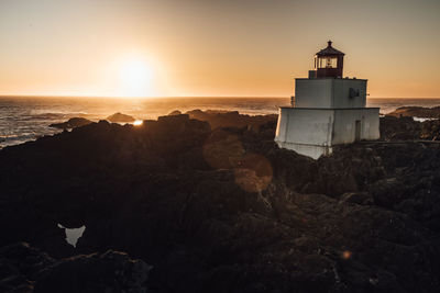 Lighthouse by sea against sky during sunset