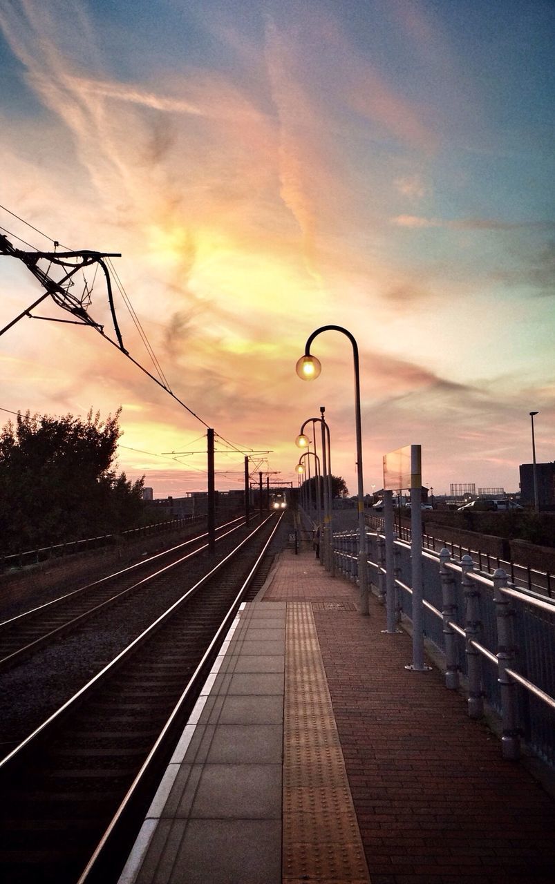 sunset, railroad track, sky, the way forward, connection, diminishing perspective, built structure, rail transportation, orange color, architecture, cloud - sky, vanishing point, power line, street light, transportation, electricity pylon, railing, building exterior, bridge - man made structure, silhouette