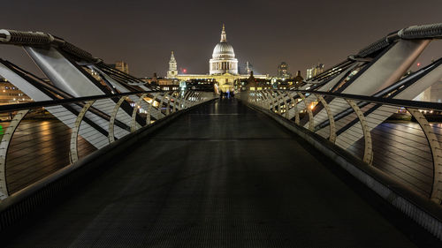 Bridge leading towards buildings in city at night