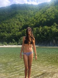 Full length of young woman in bikini standing against trees