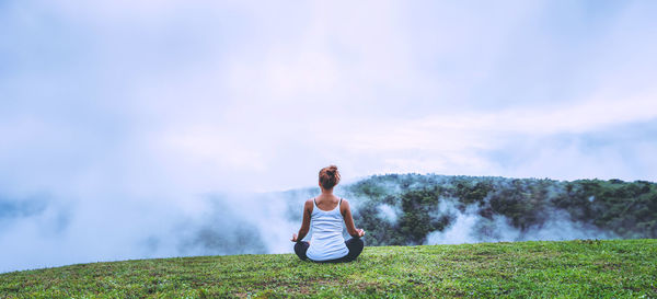 Rear view of woman sitting on mountain against sky