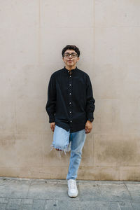 Young transgender man leaning on a wall while posing outdoors on the street.