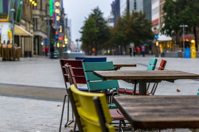 Empty chairs and tables at sidewalk cafe in city