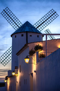 Traditional windmill by building against sky at sunset
