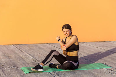 Full length of young woman using mobile phone while sitting on floor