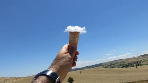 Optical illusion of man holding cloud in ice cream cone against blue sky