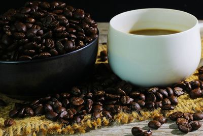 Roasted coffee beans in container by coffee cup on place mat