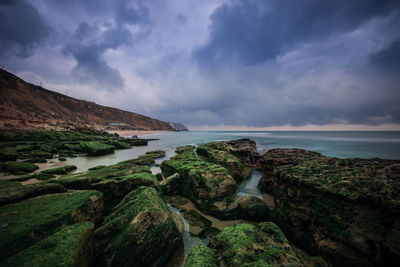 Scenic view of rock formations by sea against cloudy sky