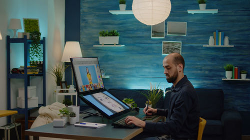 Rear view of man using laptop while sitting on table