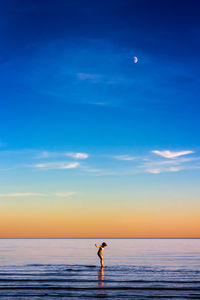 Man standing in sea against sky during sunset