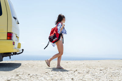 Mid adult woman carrying backpack while walking at beach during summer
