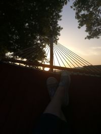 Low section of person relaxing on hammock at sunset