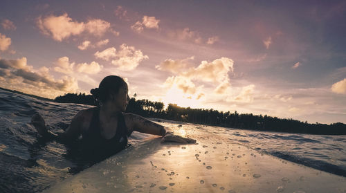 Woman sitting on beach against sky during sunset