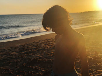 Silhouette boy standing at beach against sky during sunset