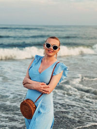 Portrait of woman wearing sunglasses while standing at beach