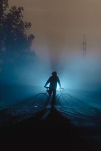 Silhouette man with bicycle standing by tree against sky