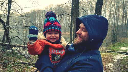 Smiling father and daughter against bare trees during winter