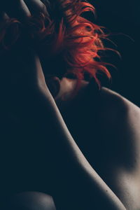 Close-up of shirtless person with dyed redhead against black background