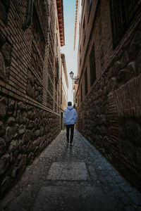 Rear view of man walking on footpath amidst buildings