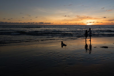 Silhouette family at beach against sky during sunset