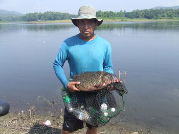 Portrait of fisherman holding fish at lake