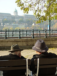 Rear view of people sitting by railing in city