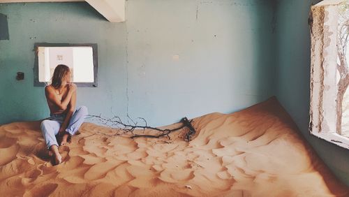 Full length of woman sitting on sand in abandoned room