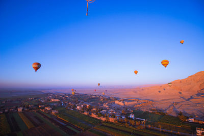 Hot air balloons flying over landscape against blue sky
