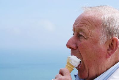 Close-up of senior man eating ice cream against blue sky