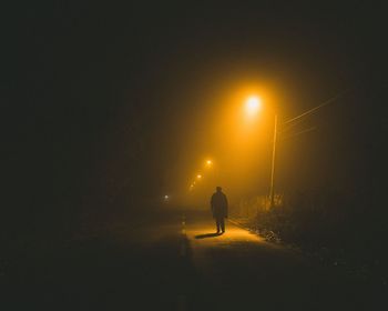 Silhouette person on illuminated street against sky at night