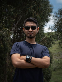 Portrait of young man wearing sunglasses standing against trees